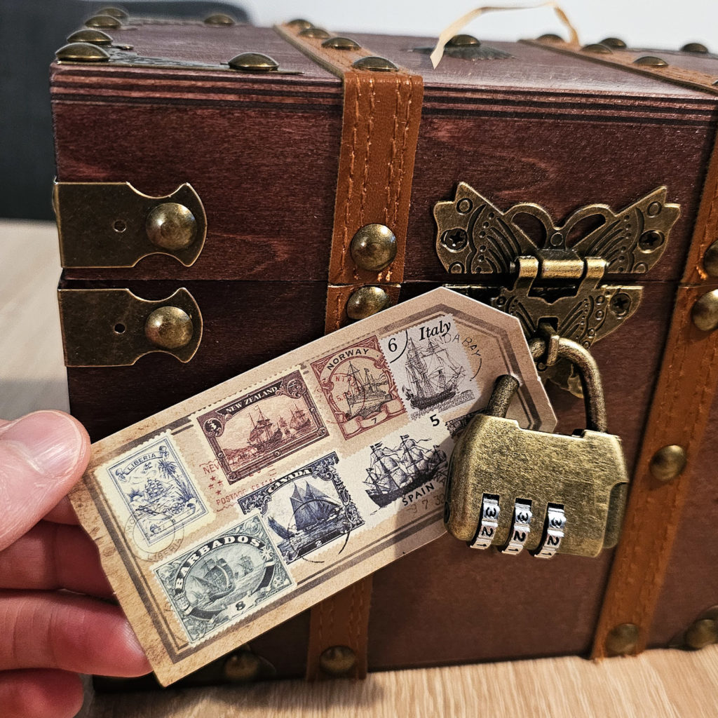 A wooden box locked with a three digit number lock, with a label bearing stamps attached