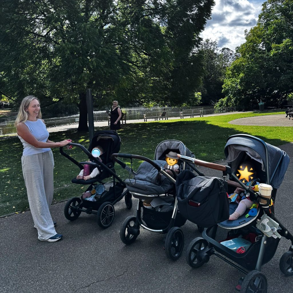 Three prams in a park with a woman stood next to them, and Becky stood further in the distance